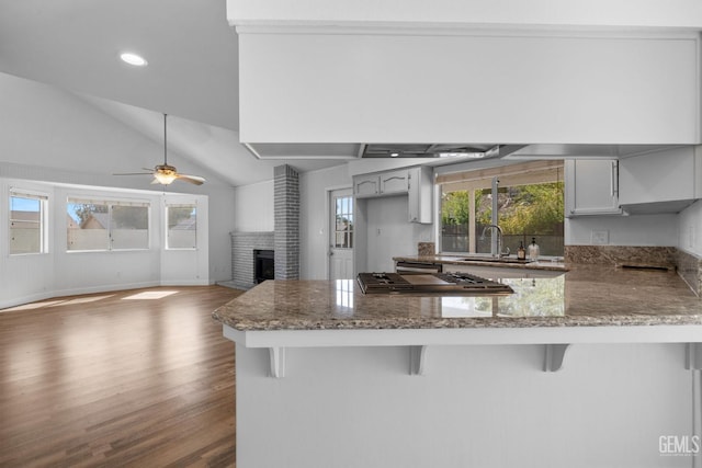 kitchen featuring a sink, a kitchen breakfast bar, wood finished floors, a peninsula, and stone counters