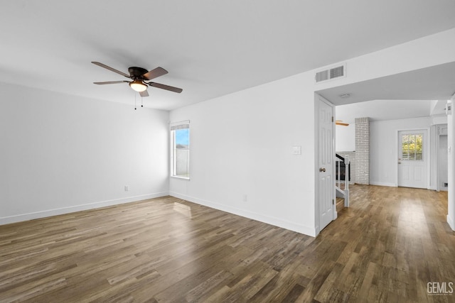 empty room featuring a ceiling fan, wood finished floors, visible vents, baseboards, and a fireplace