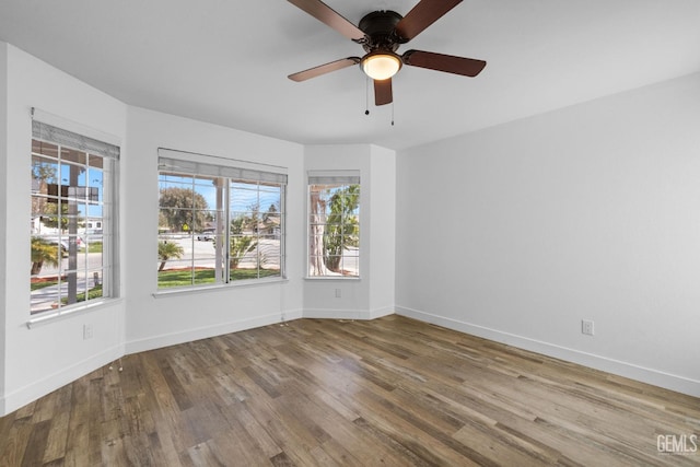 empty room featuring baseboards, plenty of natural light, wood finished floors, and a ceiling fan