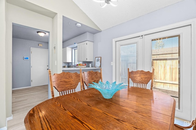 dining room featuring vaulted ceiling, a textured ceiling, light wood-type flooring, and baseboards