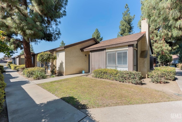 view of front of property with a chimney, a front lawn, and stucco siding