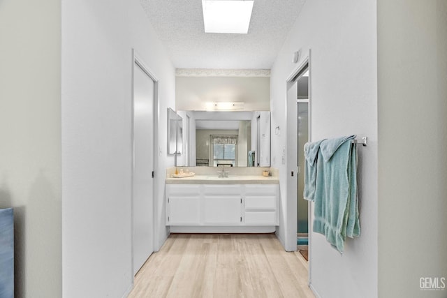 full bath featuring a skylight, a stall shower, wood finished floors, a textured ceiling, and vanity