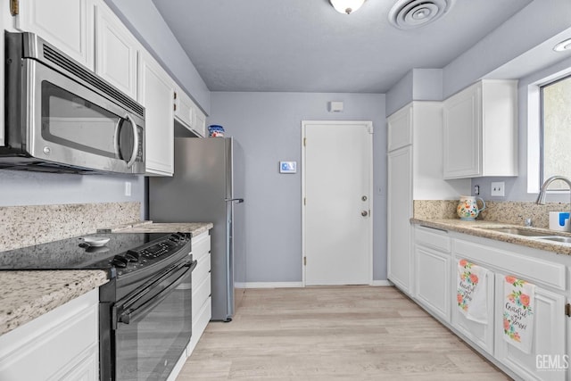 kitchen featuring black / electric stove, stainless steel microwave, a sink, and white cabinets