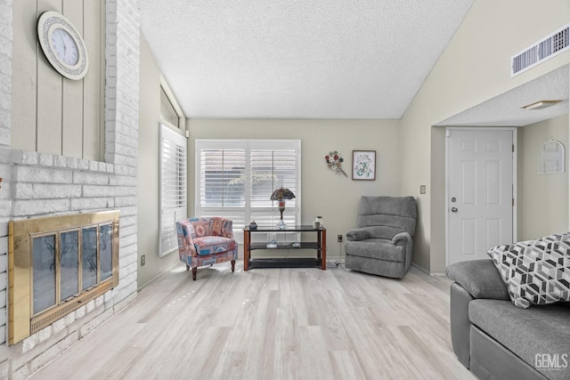 living room with lofted ceiling, visible vents, a brick fireplace, a textured ceiling, and wood finished floors