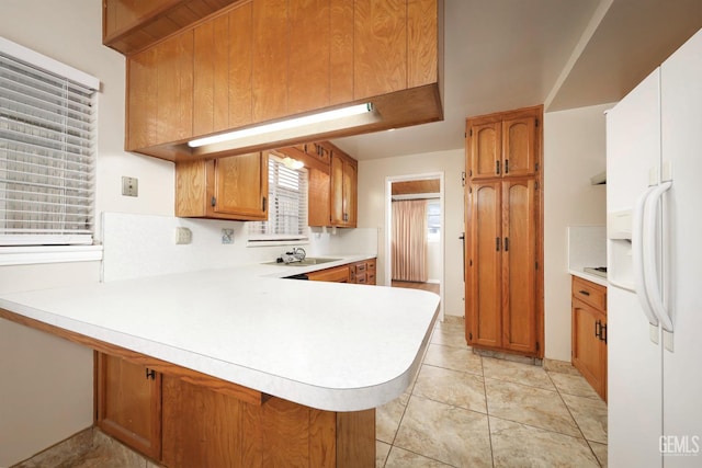 kitchen featuring a peninsula, white fridge with ice dispenser, light countertops, and a sink