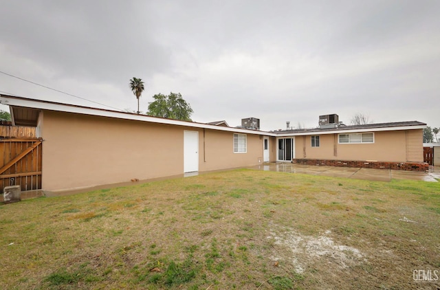 rear view of property featuring central AC, a lawn, fence, and stucco siding