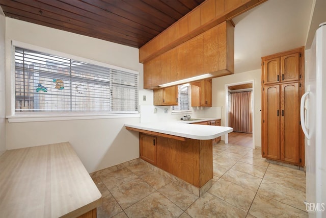 kitchen featuring a breakfast bar, light countertops, brown cabinetry, freestanding refrigerator, and a peninsula