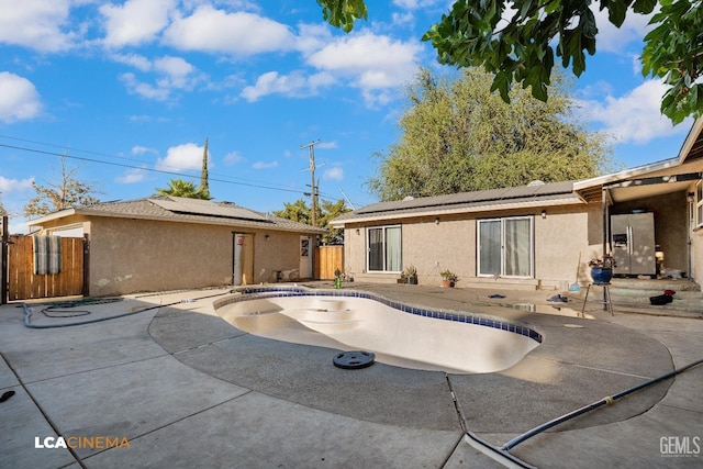 back of property featuring stucco siding, roof mounted solar panels, a patio area, and an empty pool