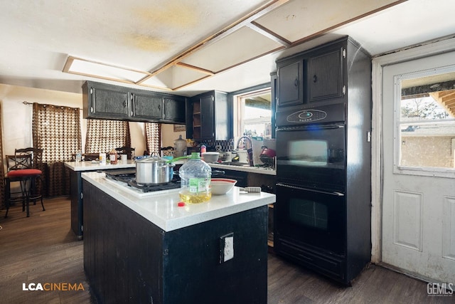 kitchen with plenty of natural light, dobule oven black, dark cabinets, and light countertops