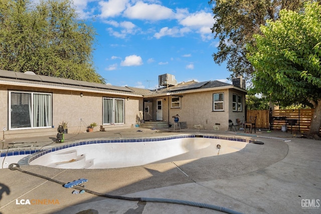 back of house featuring central AC unit, fence, stucco siding, solar panels, and an empty pool