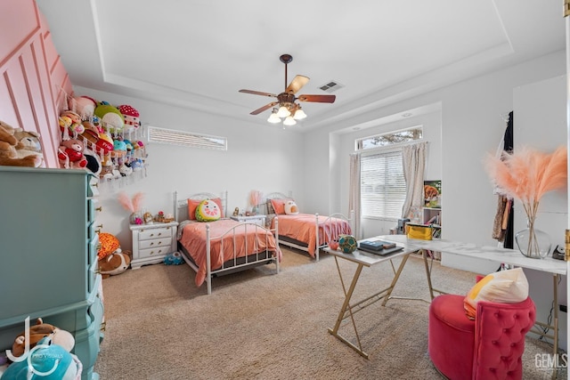 carpeted bedroom with a raised ceiling, visible vents, and ceiling fan