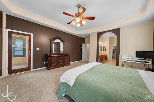 bedroom with a tray ceiling, arched walkways, baseboards, light colored carpet, and ceiling fan