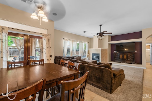 dining room with light tile patterned floors, a tile fireplace, visible vents, and ceiling fan
