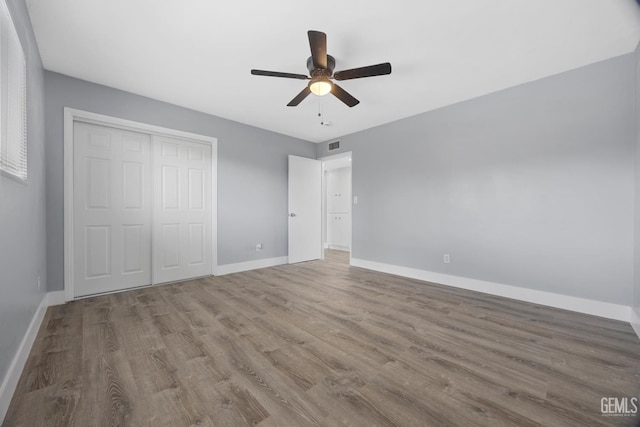 unfurnished bedroom featuring visible vents, a closet, baseboards, and wood finished floors