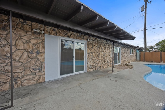 exterior space featuring stone siding, a patio, fence, and a fenced in pool