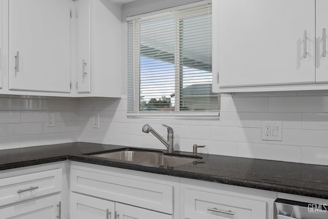 kitchen with dark stone countertops, white cabinetry, a sink, and decorative backsplash