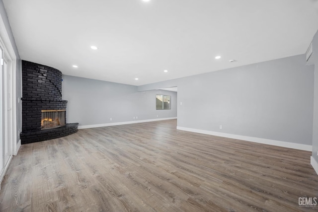 unfurnished living room featuring a brick fireplace, baseboards, wood finished floors, and recessed lighting