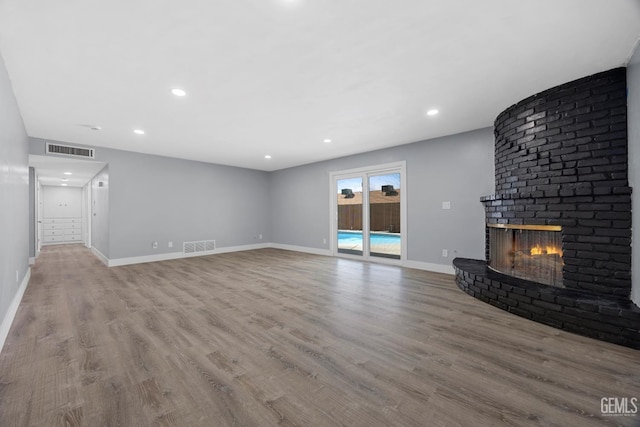 unfurnished living room with a brick fireplace, baseboards, visible vents, and wood finished floors