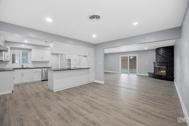 kitchen with dark countertops, light wood-style flooring, stainless steel dishwasher, open floor plan, and white cabinetry