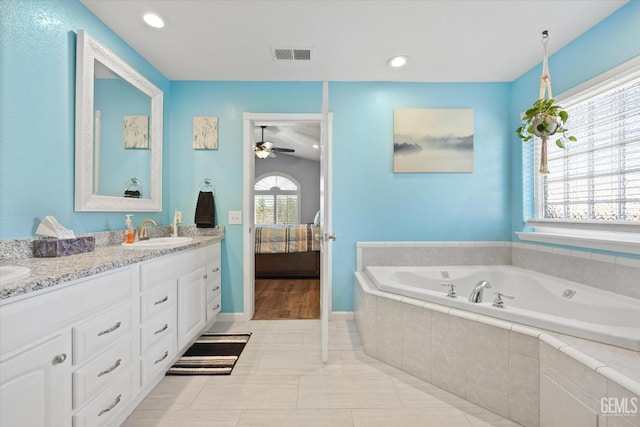 bathroom with tile patterned flooring, vanity, tiled bath, and ceiling fan