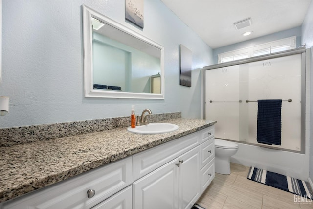 full bathroom featuring vanity, shower / bath combination with glass door, and toilet