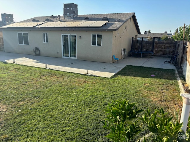 back of property with a trampoline, a fenced backyard, a yard, and stucco siding