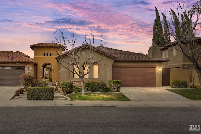 mediterranean / spanish house featuring a tile roof, driveway, an attached garage, and stucco siding