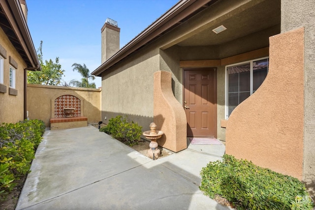 entrance to property featuring a chimney, a patio area, a gate, and stucco siding