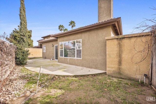 back of house featuring stucco siding, a chimney, fence, and a patio