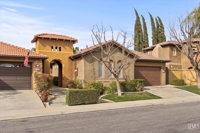 mediterranean / spanish house featuring concrete driveway, a tile roof, an attached garage, and stucco siding