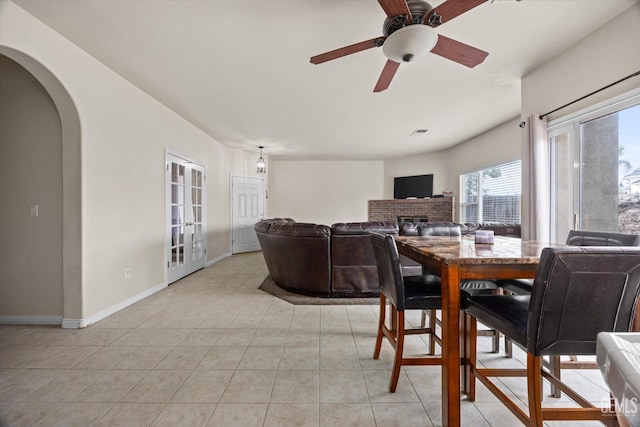 dining space featuring arched walkways, light tile patterned floors, visible vents, a ceiling fan, and baseboards