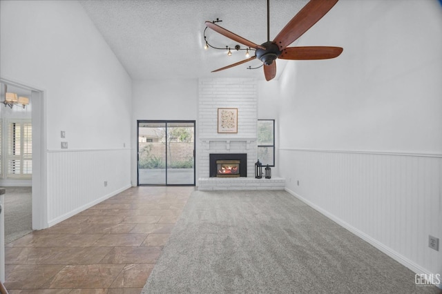 unfurnished living room with a textured ceiling, wainscoting, a fireplace, and high vaulted ceiling