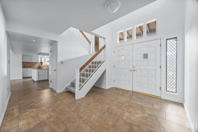 entrance foyer featuring stairs, stone finish flooring, and baseboards