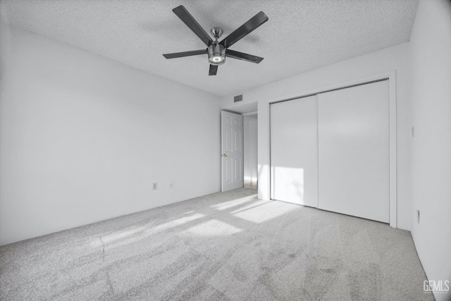 unfurnished bedroom with a closet, visible vents, a ceiling fan, carpet flooring, and a textured ceiling