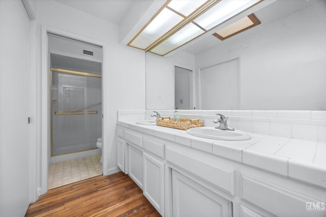 bathroom with a stall shower, double vanity, a sink, and wood finished floors