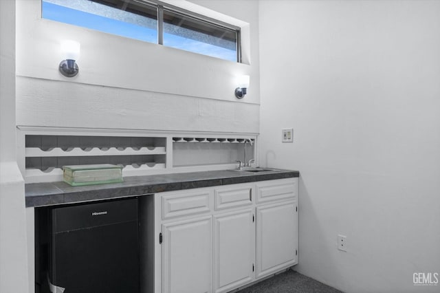 interior space with refrigerator, dark countertops, white cabinetry, a sink, and carpet flooring