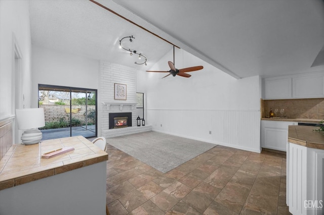 unfurnished living room with a wainscoted wall, a fireplace, lofted ceiling, a ceiling fan, and a textured ceiling