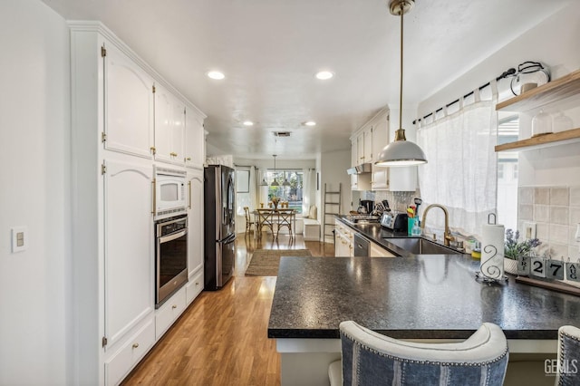 kitchen with hardwood / wood-style floors, sink, appliances with stainless steel finishes, decorative light fixtures, and kitchen peninsula