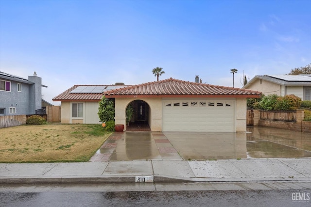 view of front facade with a garage, driveway, a tiled roof, fence, and roof mounted solar panels