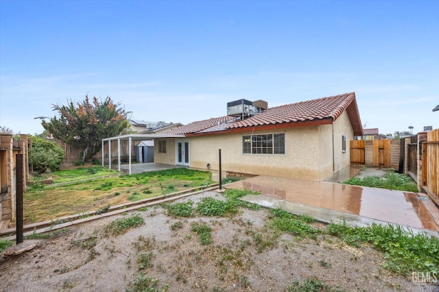 back of property with french doors, a tile roof, stucco siding, a patio area, and a fenced backyard