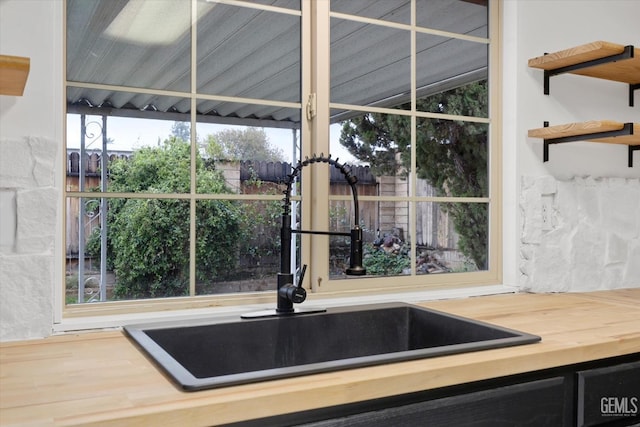 interior details with butcher block counters, a sink, dark cabinetry, backsplash, and open shelves