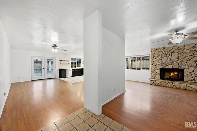 unfurnished living room with light wood-style floors, a stone fireplace, and a ceiling fan