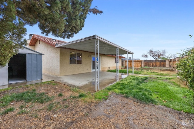 rear view of property featuring a patio, an outbuilding, fence, a shed, and stucco siding