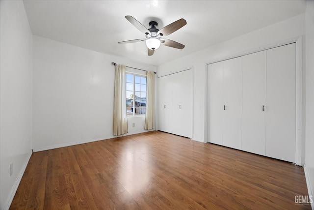 unfurnished bedroom with ceiling fan, baseboards, multiple closets, and wood finished floors