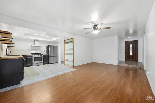 unfurnished living room featuring ceiling fan, a sink, visible vents, light wood-type flooring, and a raised ceiling