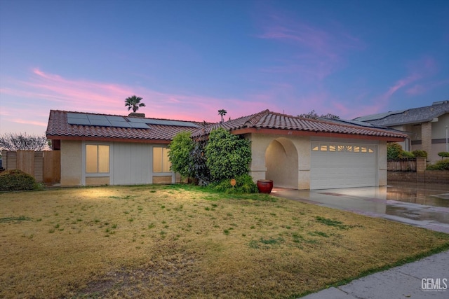 view of front facade with a garage, a tile roof, a yard, roof mounted solar panels, and stucco siding