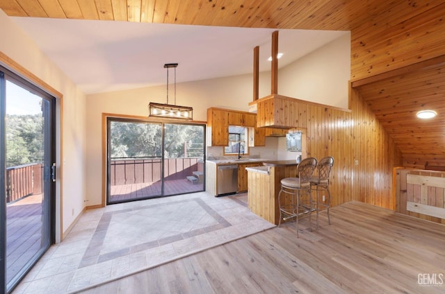 kitchen with a breakfast bar, wood walls, sink, stainless steel dishwasher, and kitchen peninsula