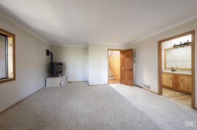 unfurnished bedroom featuring light carpet, ensuite bath, crown molding, sink, and a wood stove