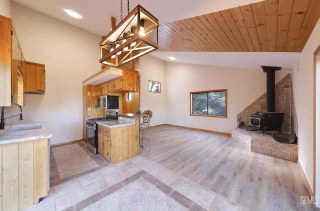 kitchen with pendant lighting, a wood stove, wooden ceiling, sink, and appliances with stainless steel finishes