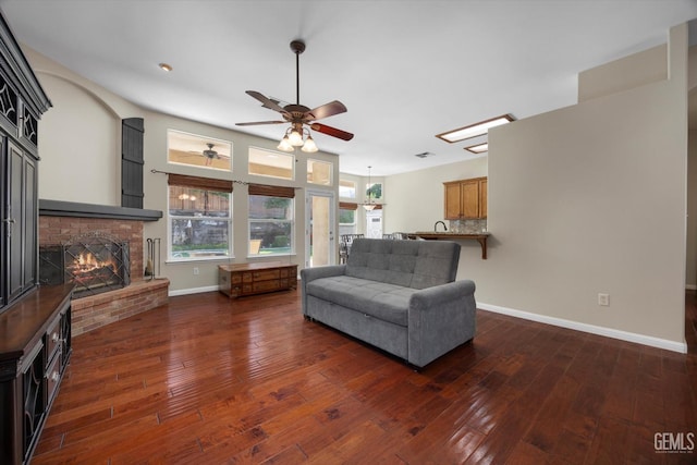 living area featuring baseboards, a fireplace, a ceiling fan, and dark wood finished floors